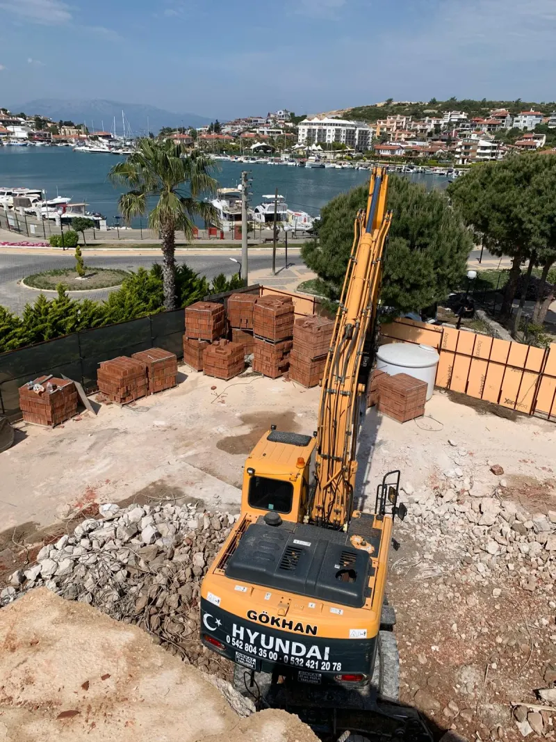 Konut inşaatında lastik tekerlekli ekskavatör, yanında tuğla paletleri